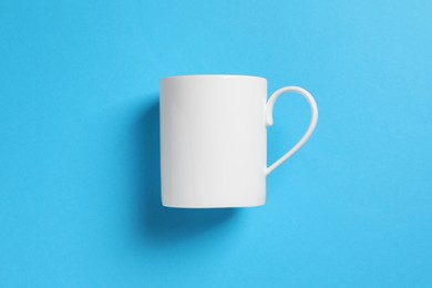 Photo of One white ceramic mug on light blue background, top view