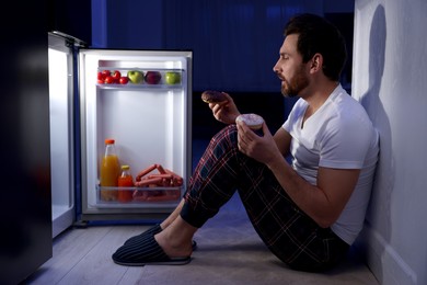 Photo of Man with donuts near refrigerator in kitchen at night. Bad habit