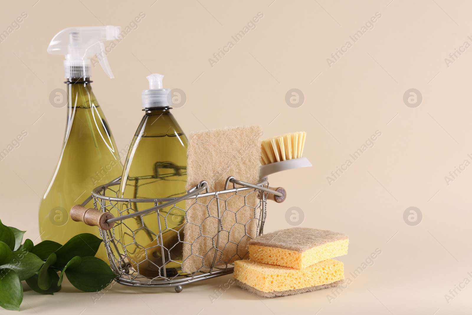 Photo of Bottles of cleaning product, sponges, brush and floral decor on beige background. Space for text