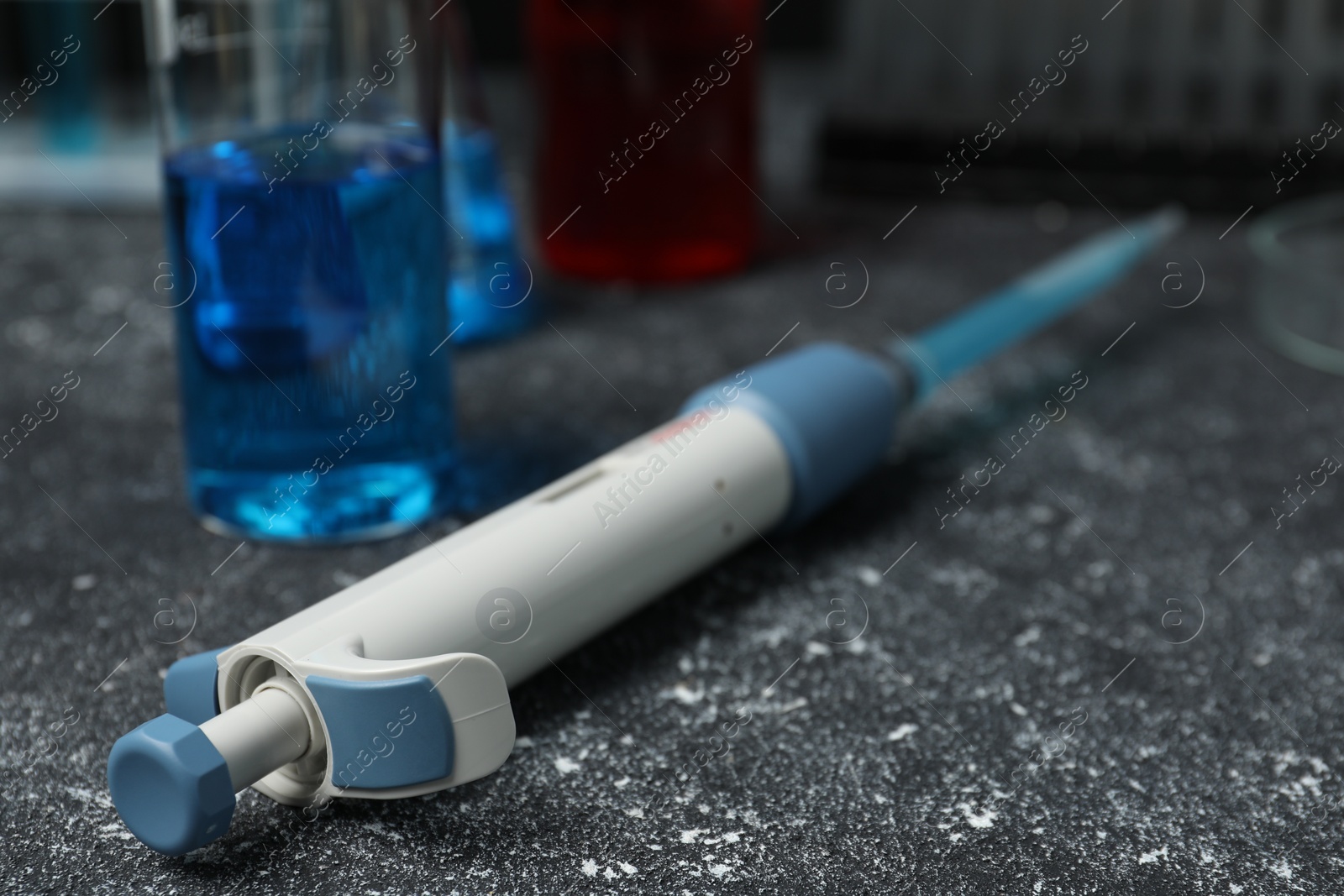 Photo of Laboratory analysis. Micropipette and beaker with liquid on grey table, closeup. Space for text