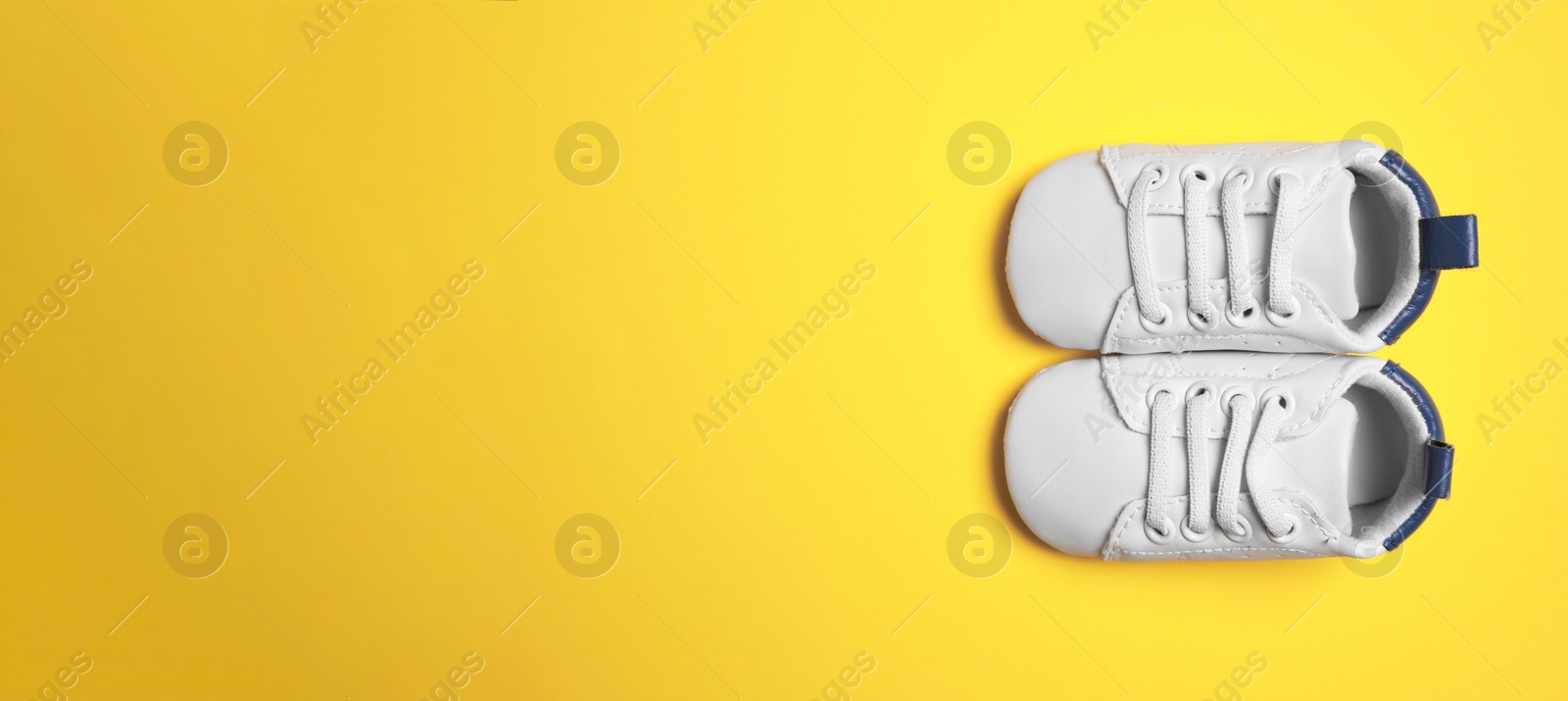 Image of Cute baby shoes on yellow background, top view. Banner design with space for text