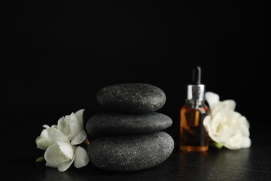 Photo of Stack of grey spa stones, flowers and oil on black table