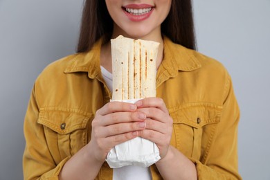 Photo of Happy young woman holding tasty shawarma on grey background, closeup