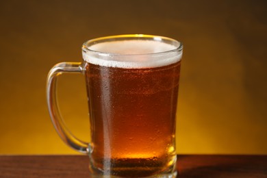 Photo of Mug with fresh beer on wooden table against dark background, closeup