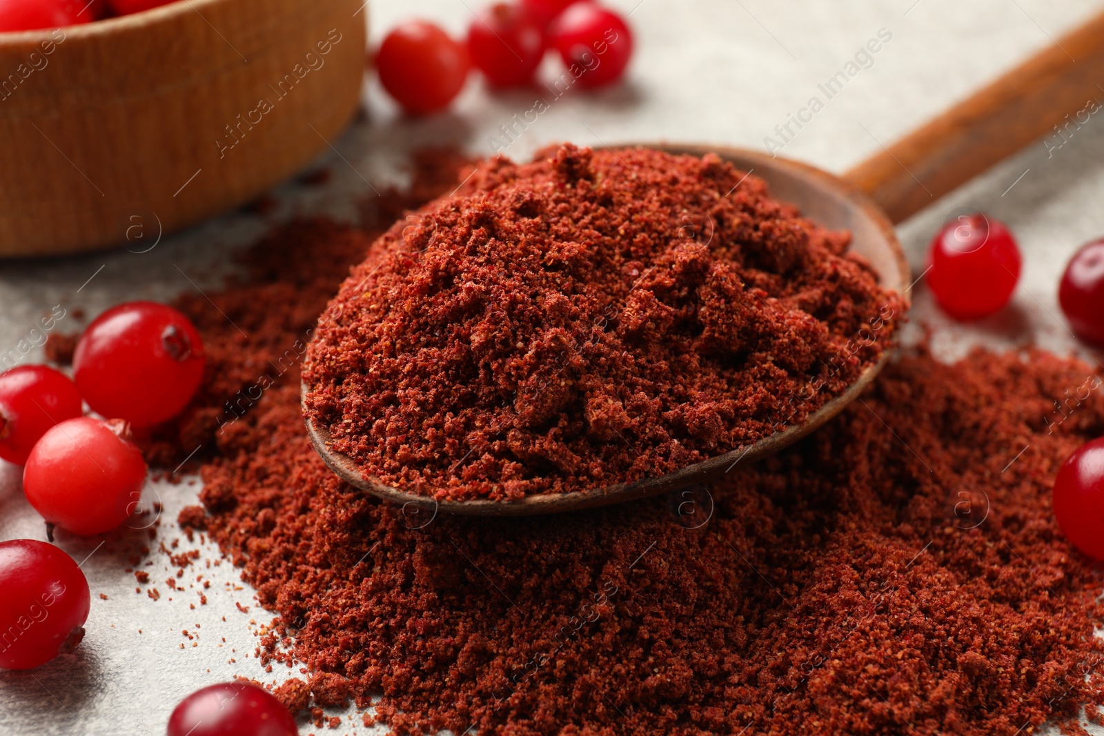 Photo of Pile of cranberry powder, spoon and fresh berries on light table, closeup