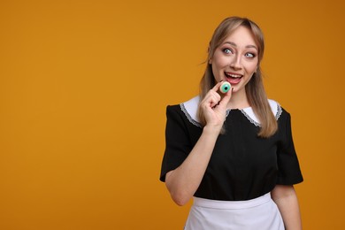 Photo of Happy woman in scary maid costume with decorative eyeball on orange background, space for text. Halloween celebration