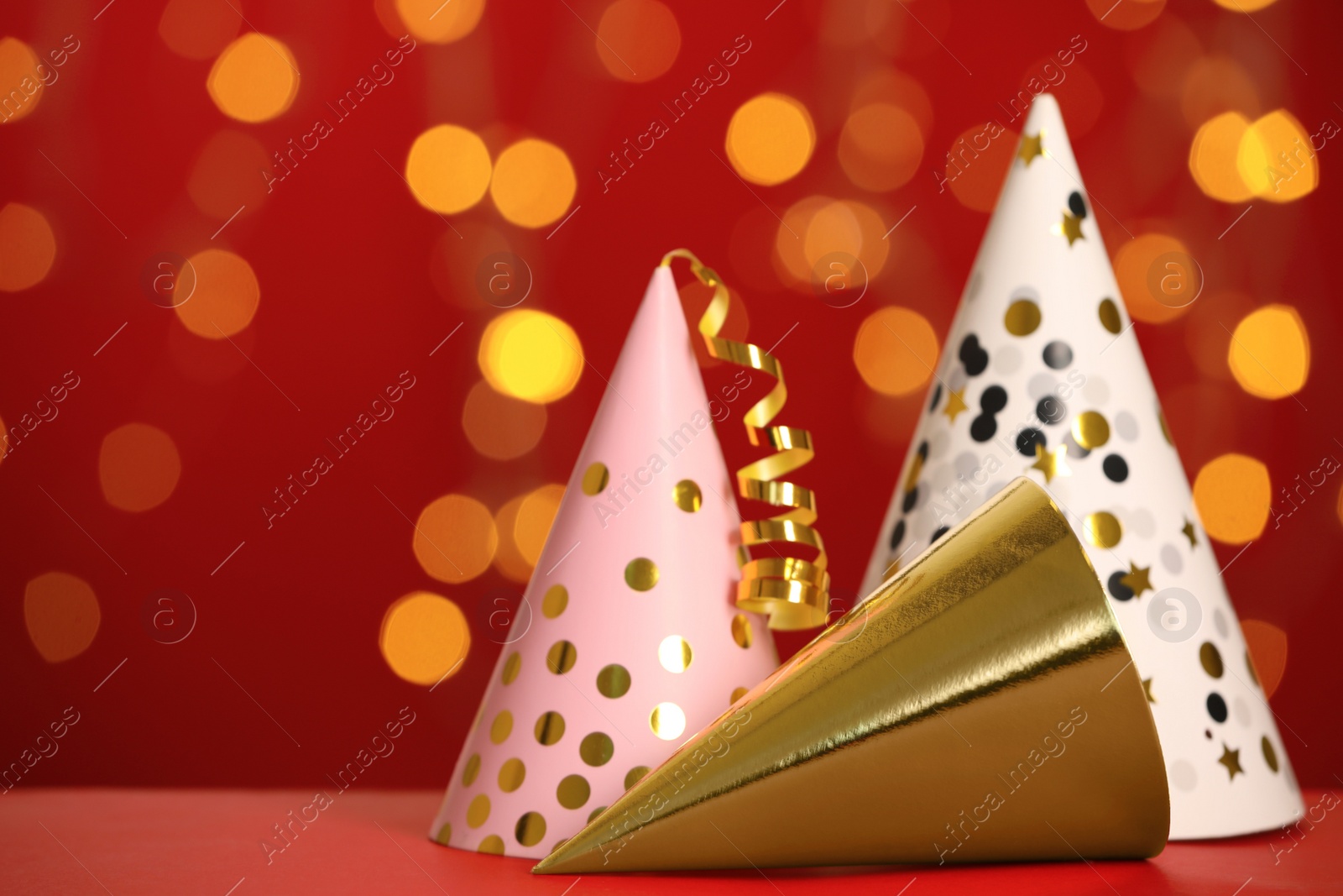 Photo of Beautiful party hats on red table against blurred festive lights. Space for text