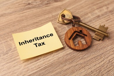 Photo of Inheritance Tax. Paper note and key with key chain in shape of house on wooden table, closeup