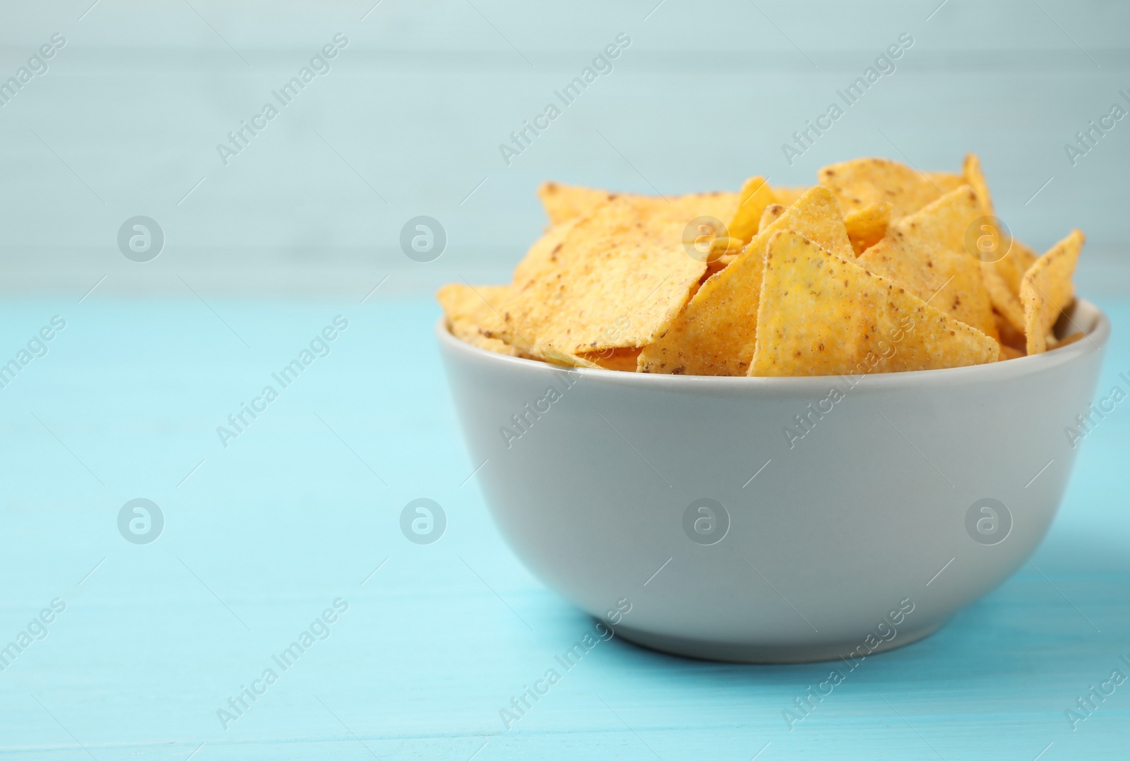 Photo of Bowl of tasty Mexican nachos chips on light blue table