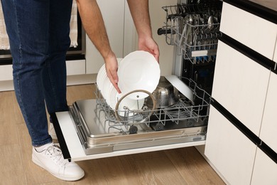 Photo of Man loading dishwasher with plates indoors, closeup