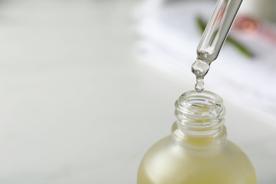Photo of Dripping hydrophilic oil into bottle on blurred background, closeup. Space for text