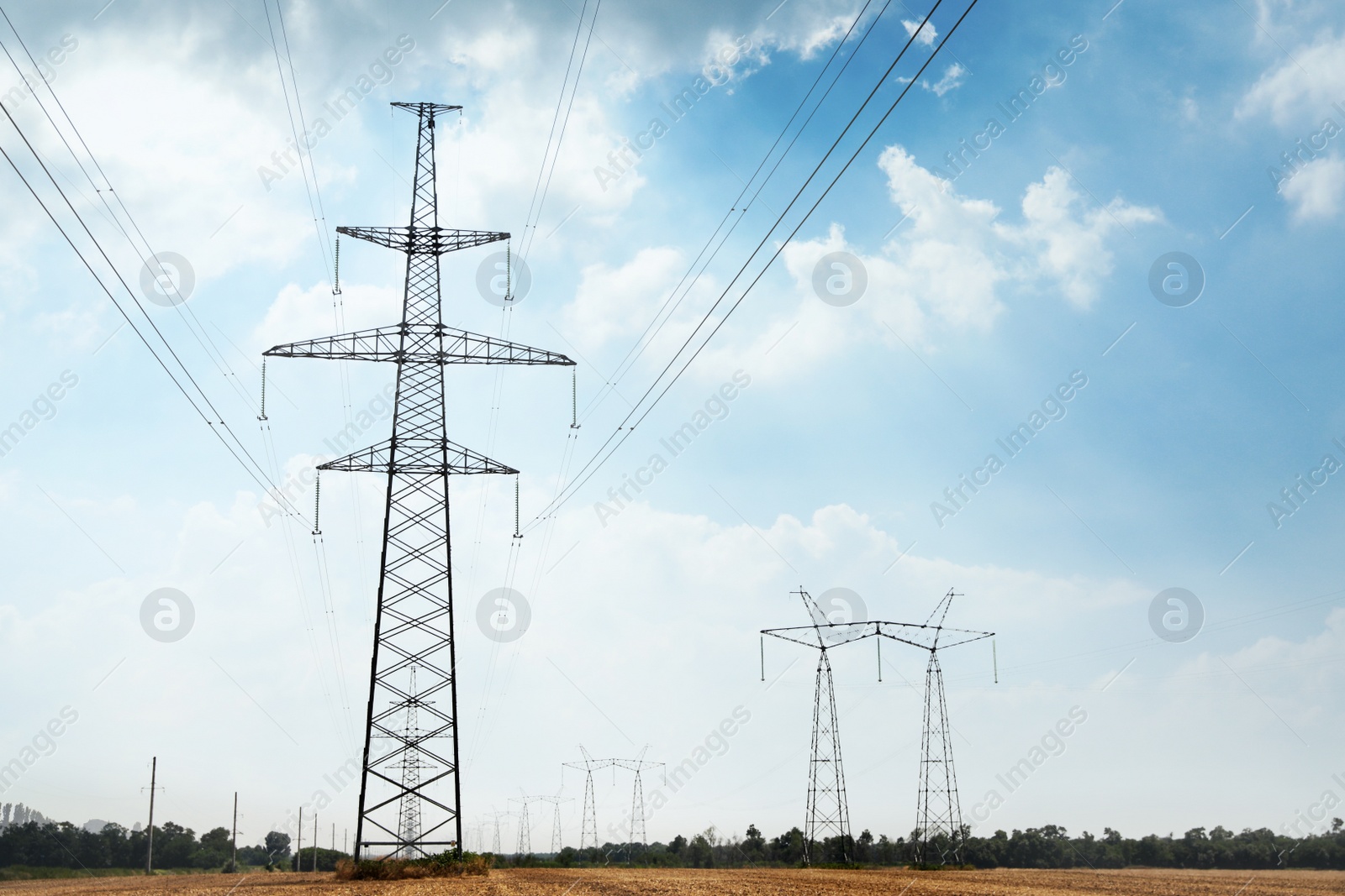 Photo of High voltage towers with electricity transmission power lines in field on sunny day