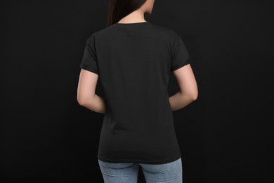 Photo of Woman wearing black t-shirt on dark background, back view