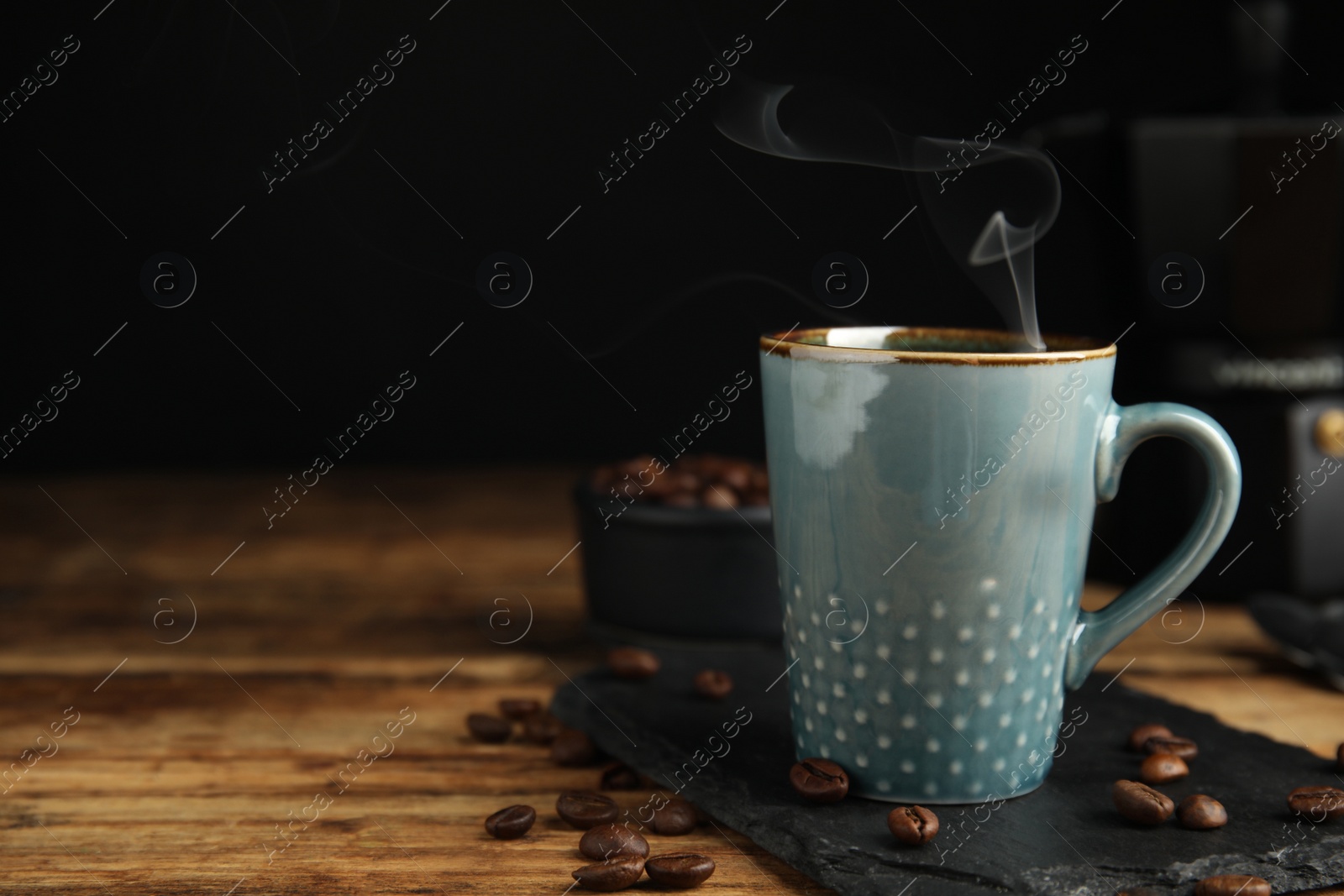 Photo of Cup of tasty coffee and beans on wooden table, space for text