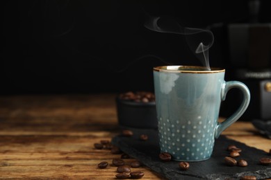 Photo of Cup of tasty coffee and beans on wooden table, space for text