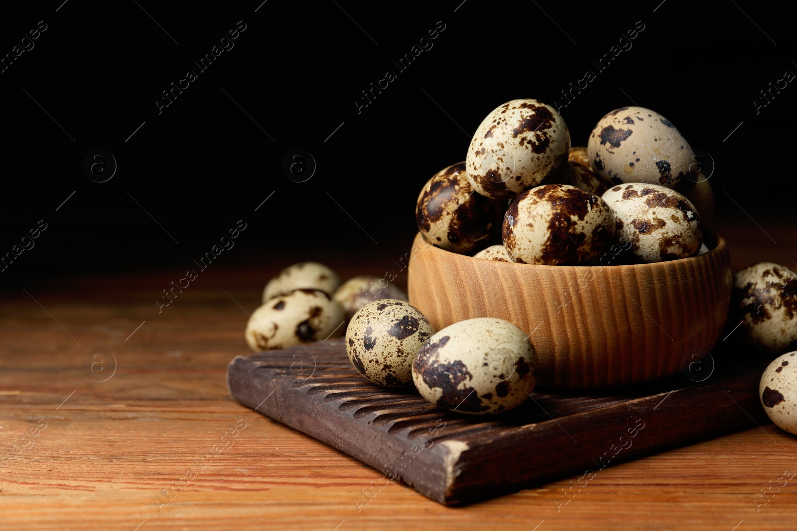 Photo of Bowl and many speckled quail eggs on wooden table. Space for text