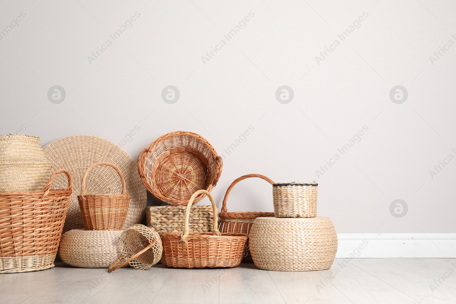 Photo of Many different wicker baskets made of natural material on floor near light wall. Space for text