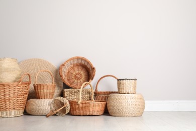 Photo of Many different wicker baskets made of natural material on floor near light wall. Space for text