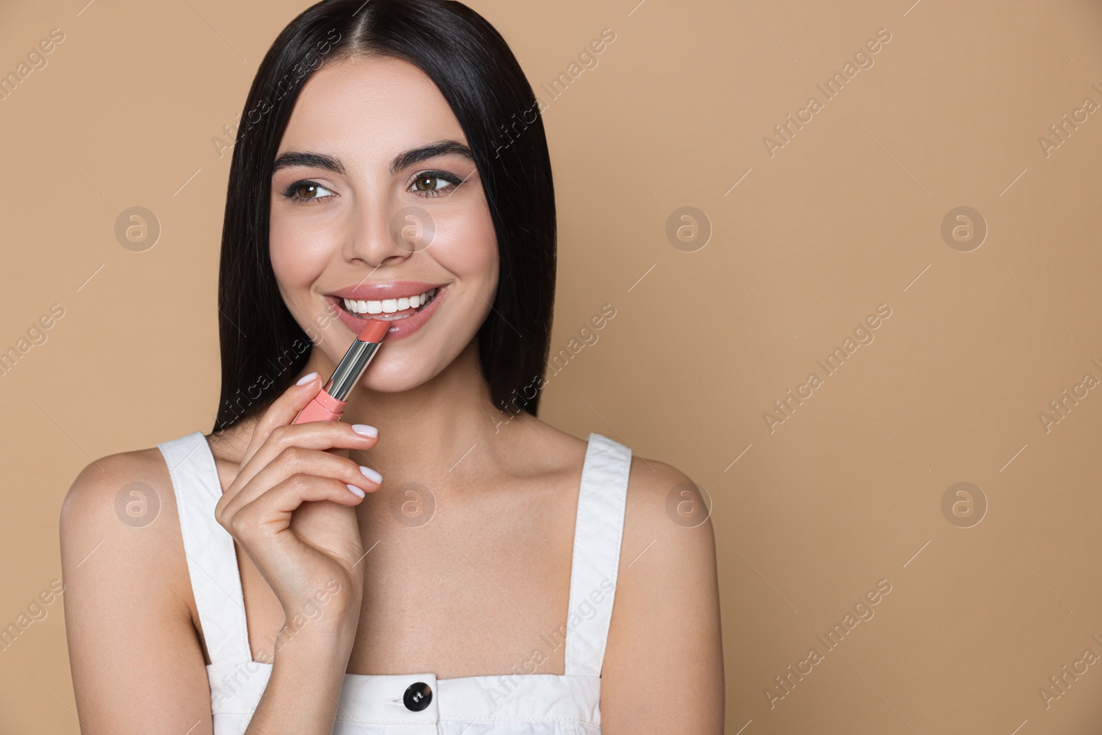 Photo of Young woman applying nude lipstick on beige background. Space for text