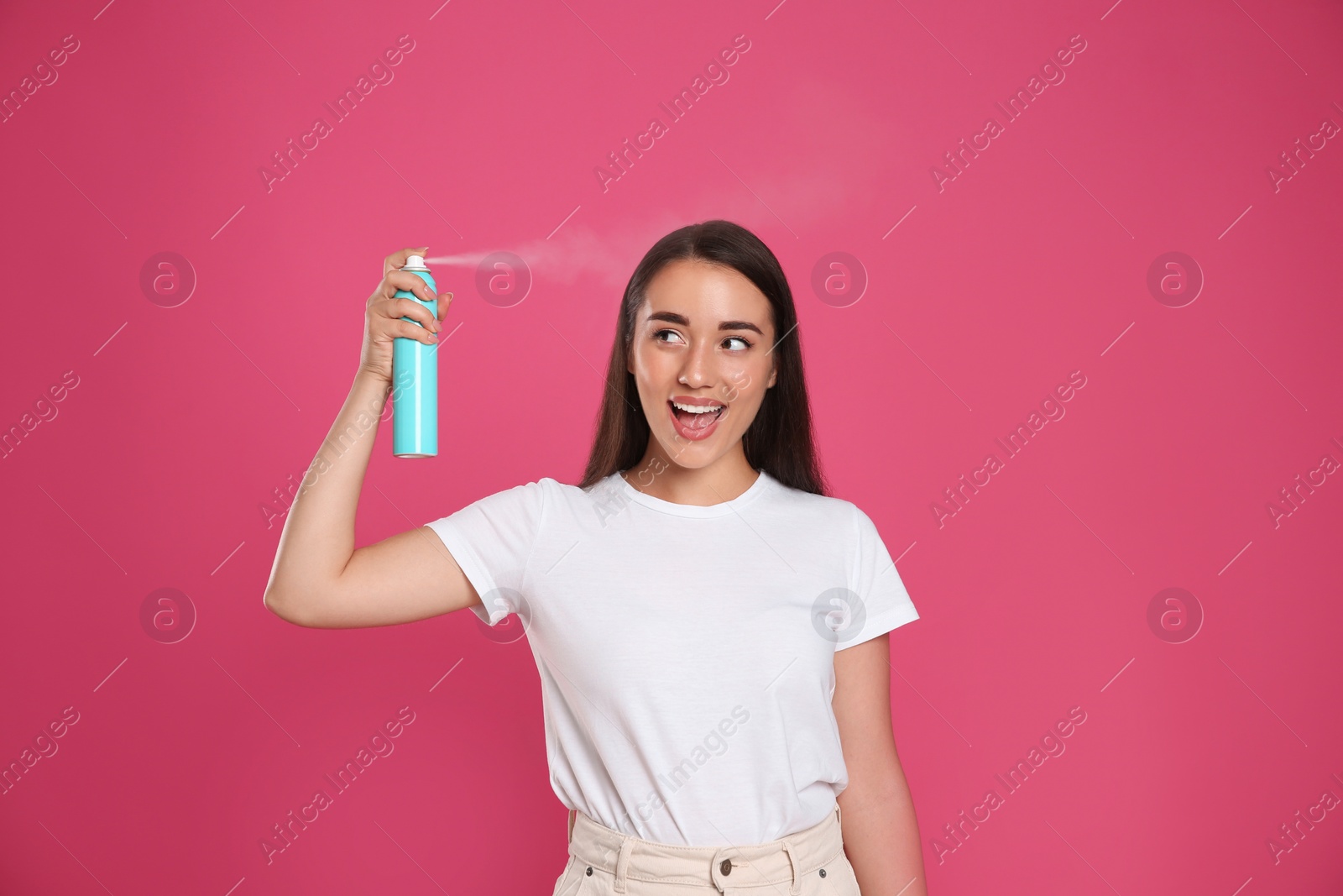 Photo of Young woman applying dry shampoo against pink background