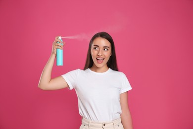 Photo of Young woman applying dry shampoo against pink background