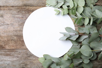 Photo of Fresh eucalyptus leaves and blank card with space for design on wooden background, top view