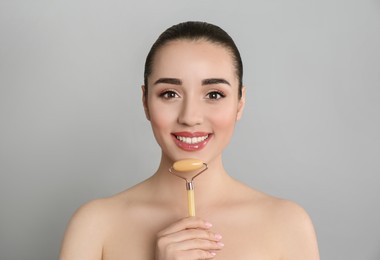 Woman using natural jade face roller on grey background