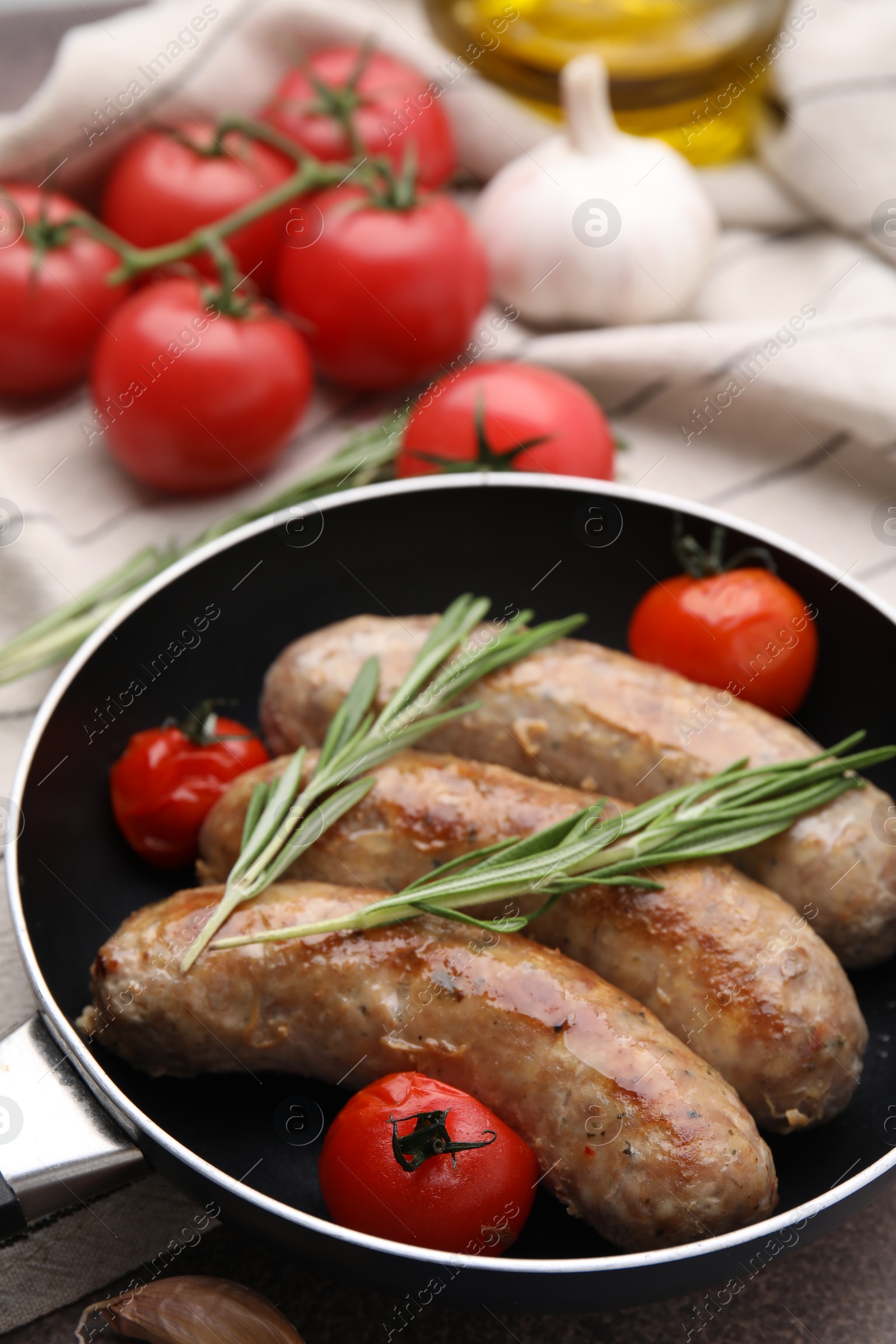 Photo of Frying pan with tasty homemade sausages, rosemary and tomatoes on table, closeup