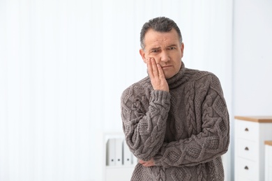 Photo of Mature man suffering from strong tooth pain at home, space for text