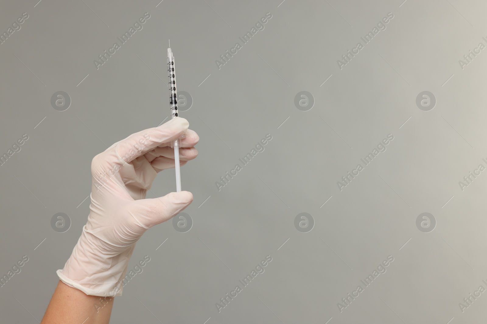 Photo of Doctor holding medical syringe on grey background, closeup. Space for text