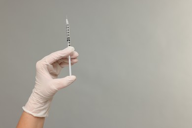 Photo of Doctor holding medical syringe on grey background, closeup. Space for text