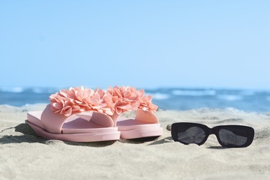 Photo of Stylish slippers and sunglasses on sandy beach near sea