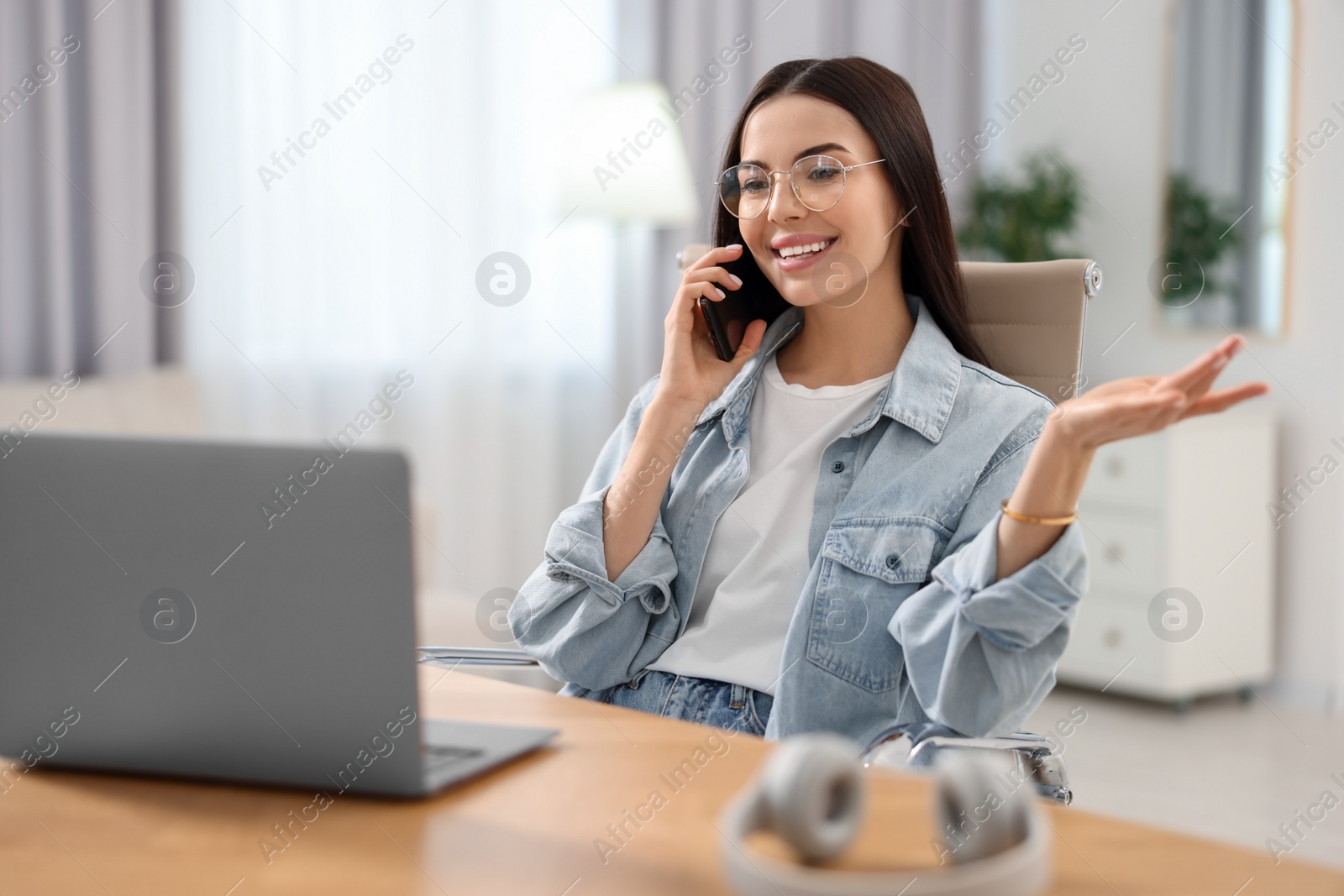 Photo of Young woman talking on smartphone during webinar at table in room