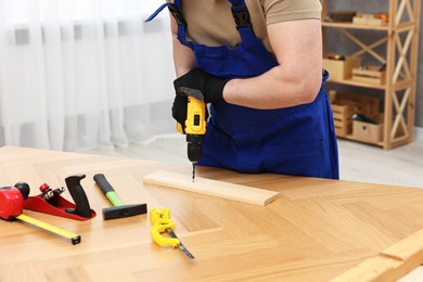 Young worker using electric drill at table in workshop, closeup