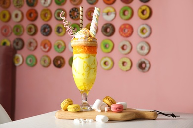 Photo of Tasty milk shake with sweets in glass and macarons served on table indoors