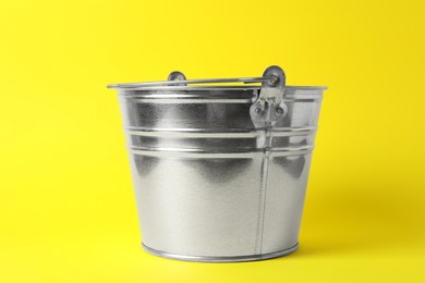 Photo of One shiny metal bucket on yellow background