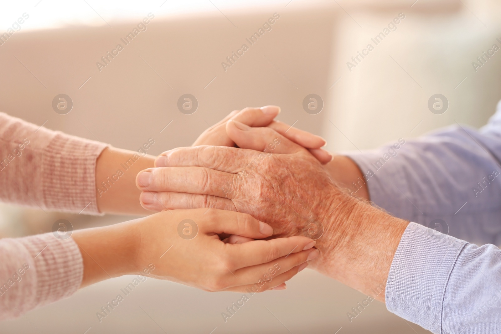 Photo of Young woman holding elderly man hands indoors, closeup. Help service