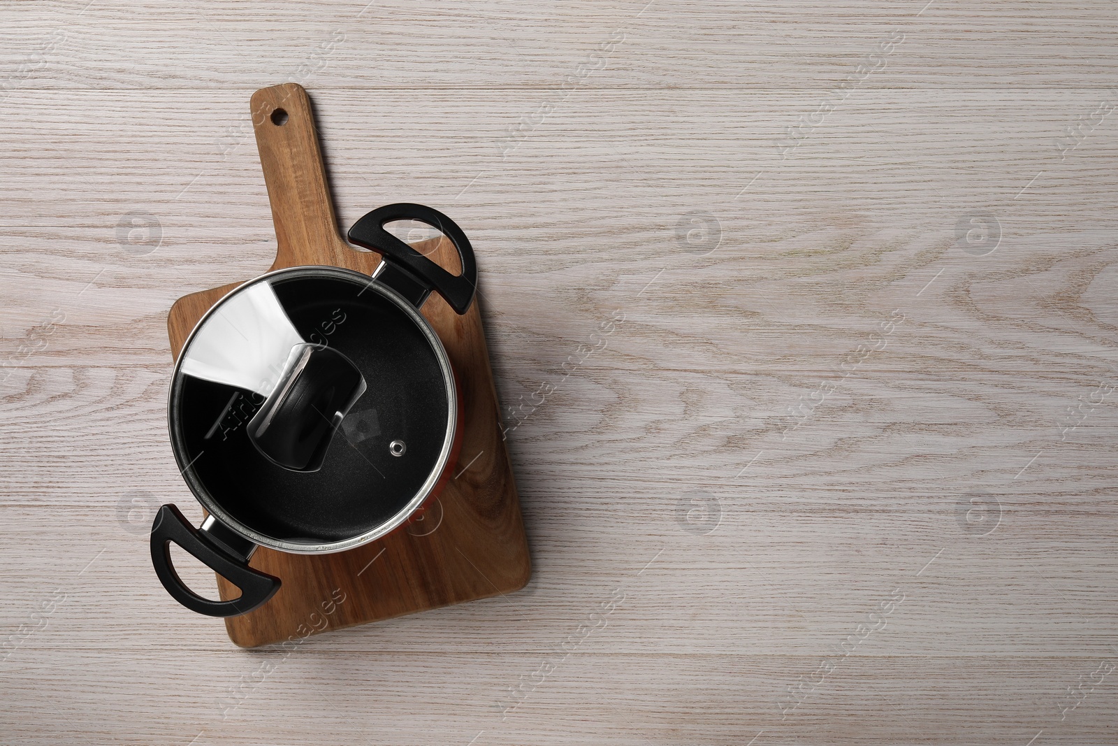 Photo of Black pot with glass lid on white wooden table, top view. Space for text