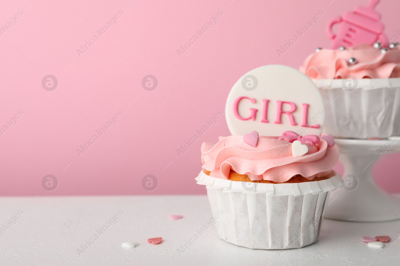 Photo of Baby shower cupcakes with toppers on white table against pink background, space for text