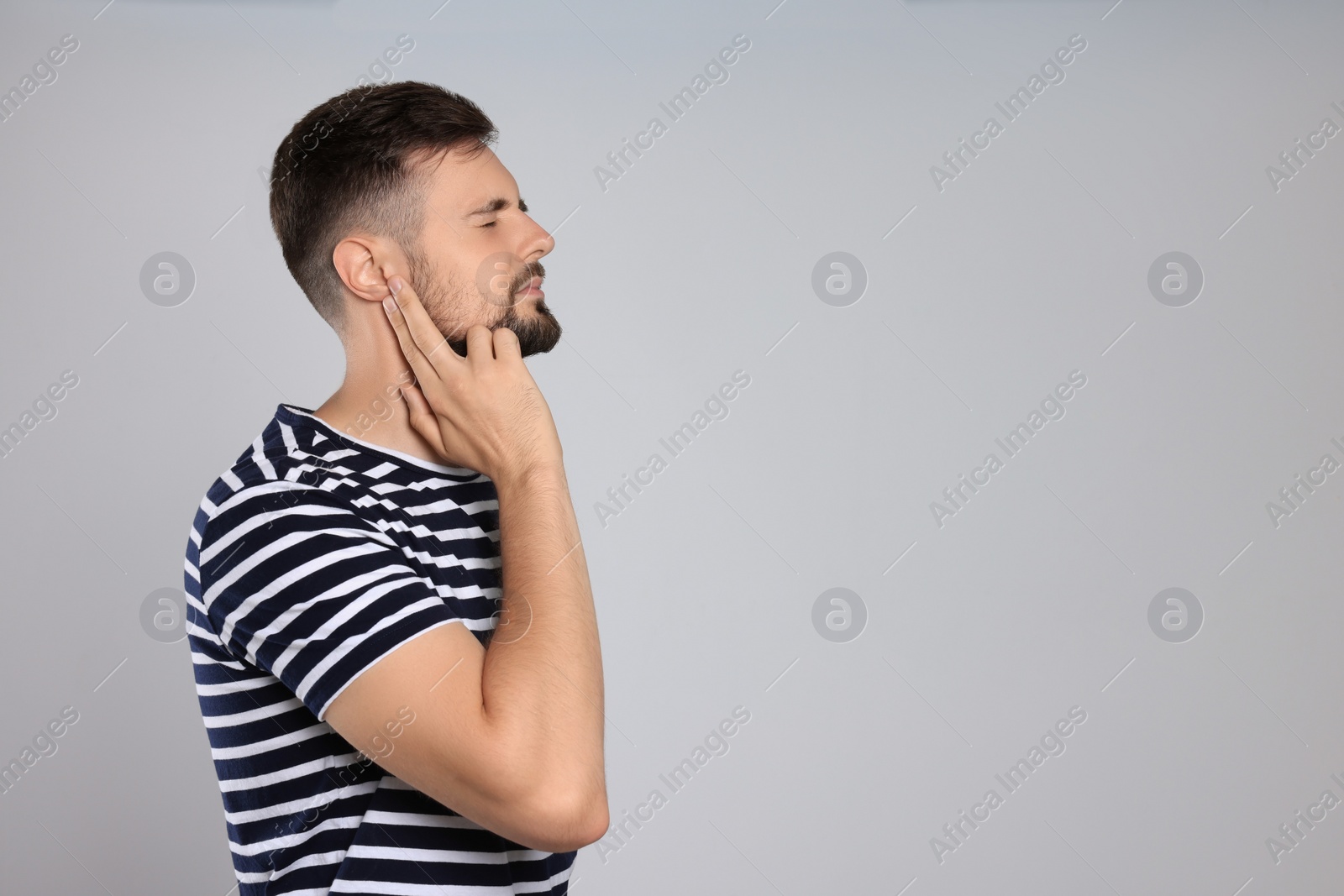 Photo of Young man suffering from ear pain on light grey background. Space for text