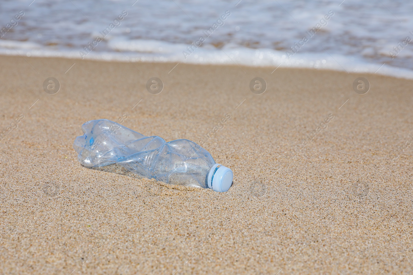 Photo of Used plastic bottle on sand near water. Recycling problem