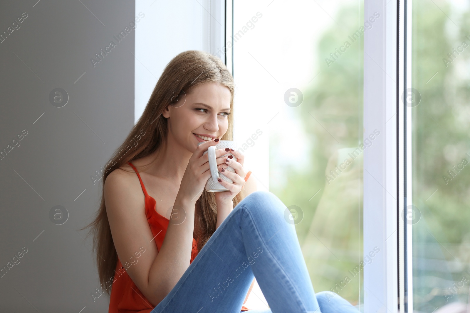 Photo of Young beautiful woman drinking morning coffee near window at home