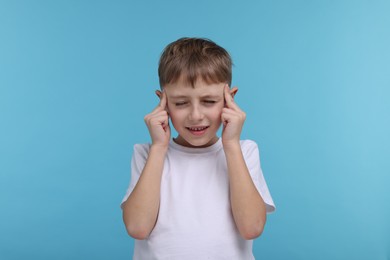 Photo of Little boy suffering from headache on light blue background