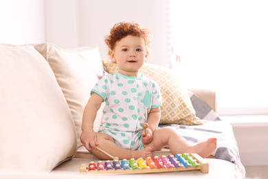 Photo of Cute little child playing with xylophone on sofa at home