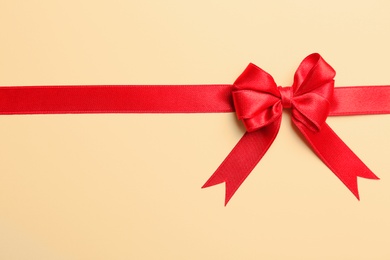 Photo of Red ribbon with bow on color background, top view