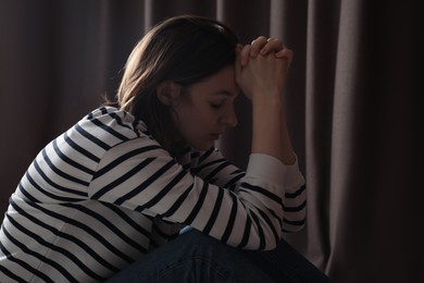 Sad young woman near closed curtains indoors