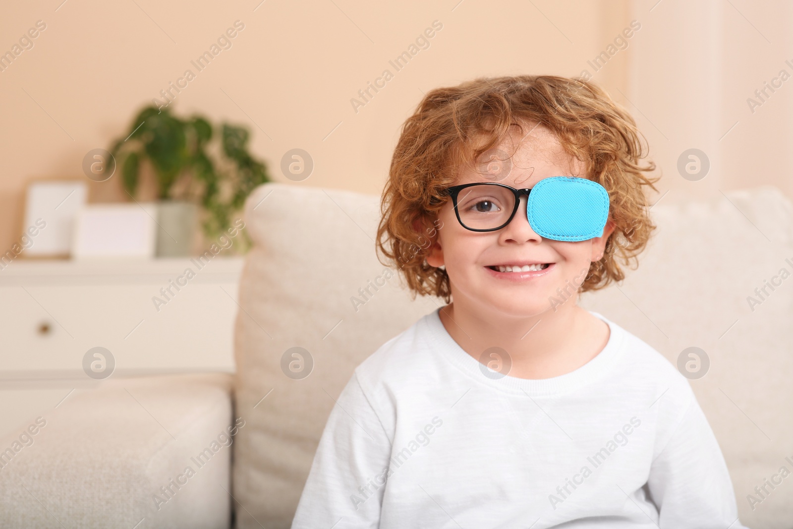 Photo of Happy boy with eye patch on glasses indoors, space for text. Strabismus treatment