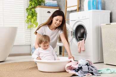 Photo of Happy mother with her daughter having fun while washing baby clothes in bathroom