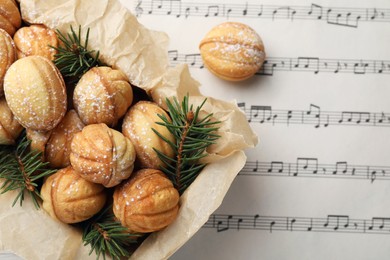 Photo of Homemade walnut shaped cookies with powdered sugar and fir branches in box on note sheet, flat lay. Space for text