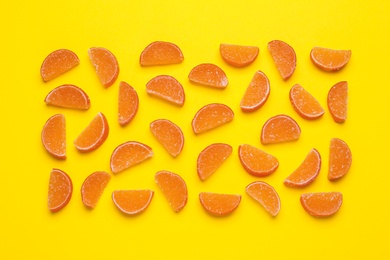 Photo of Delicious orange marmalade candies on yellow background, flat lay